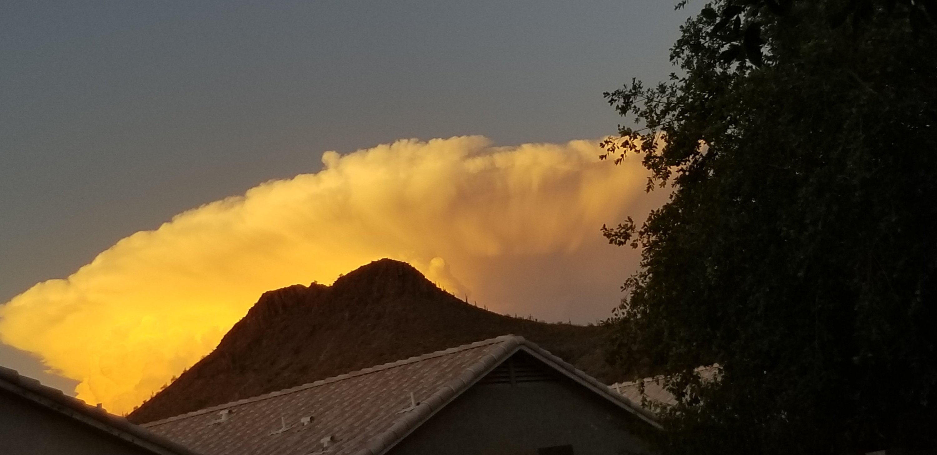 Cumulus cloud illuminated by sunset nears mountain